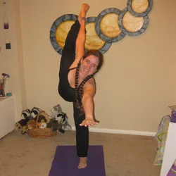 Jolynn doing a standing yoga pose, one leg raised straight up, in front of an abstract painting by Thad.