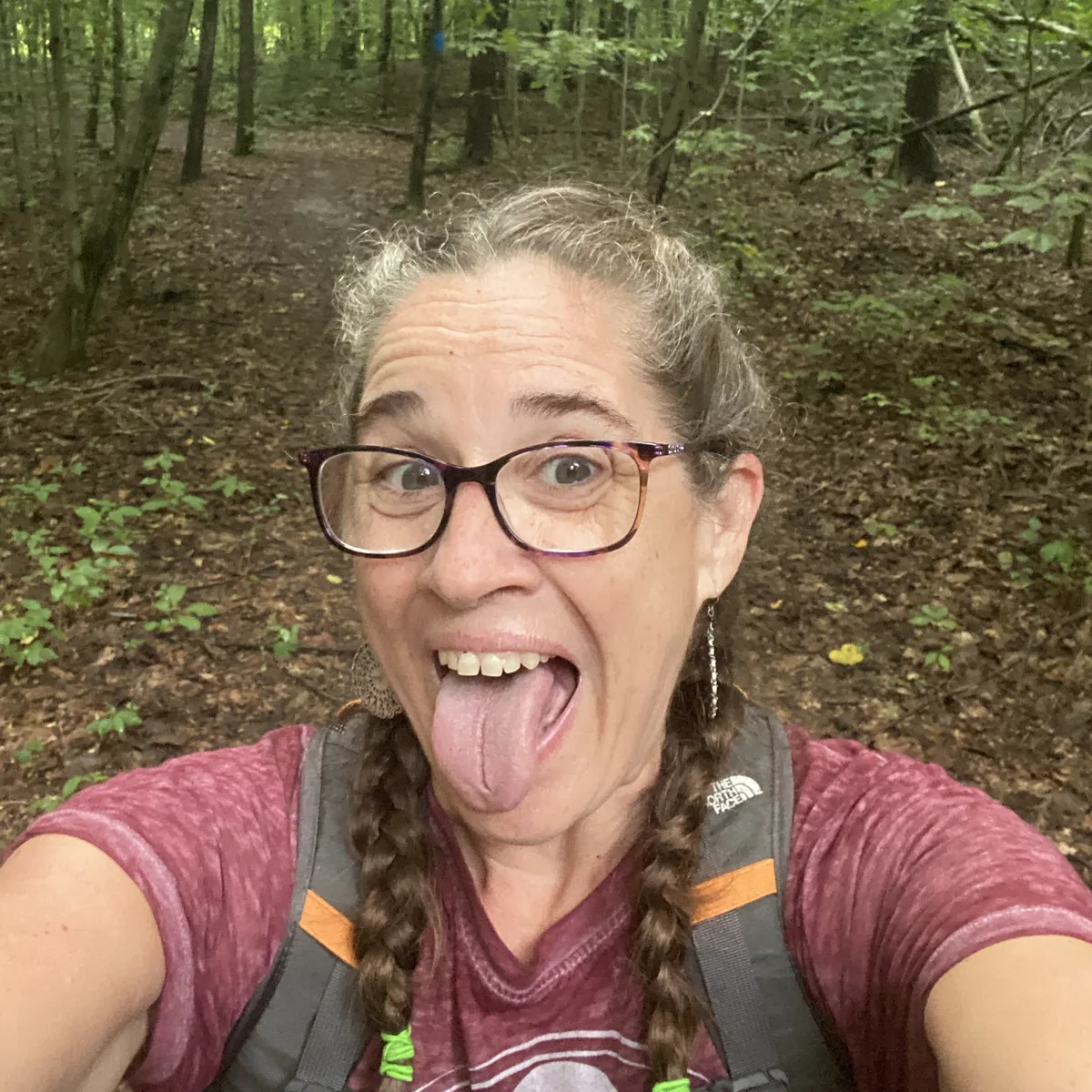 Jolynn making a goofy face on a wooded hiking trail, wearing a backpack.