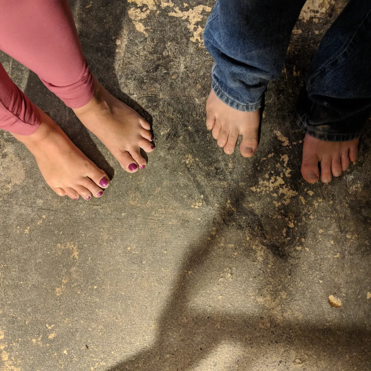 Jolynn and Ando's bare feet side by side on a weathered concrete floor.